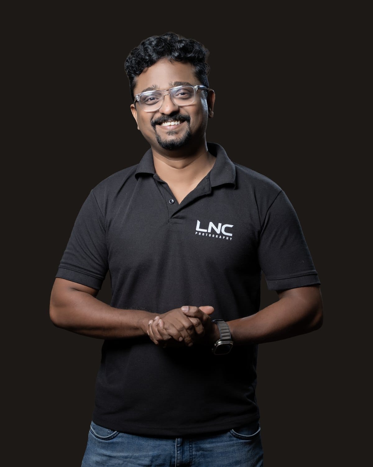 Abbishek Abraham John, founder of LNC Photography, in a black LNC polo against a dark studio backdrop