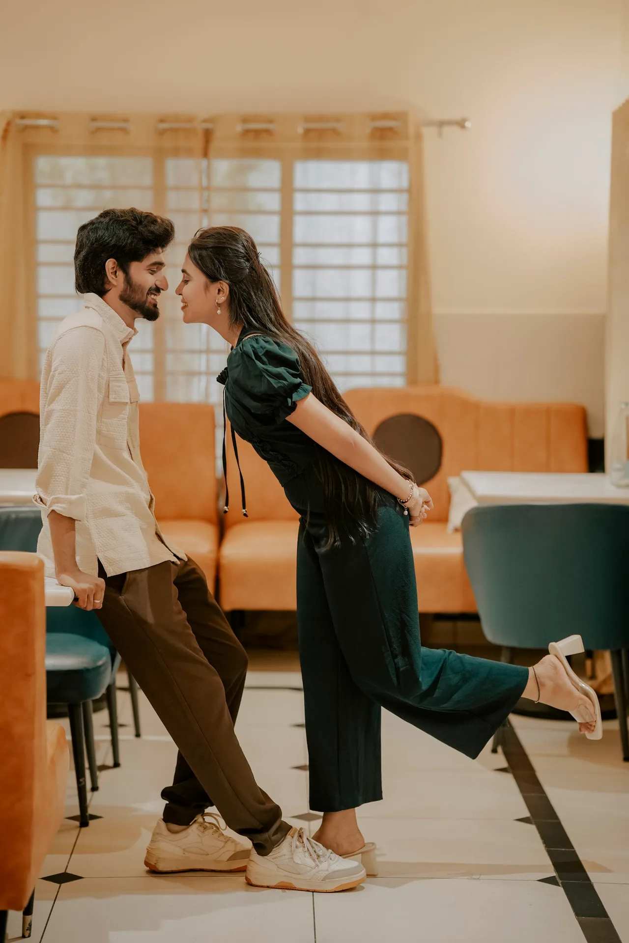Playful pre-wedding moment in a retro café with orange sofas at Bristograph, Adyar, Chennai — LNC Photography.
